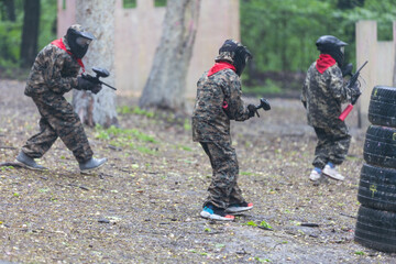 Paintball game. Players with weapons shooting paint balls. Men on the playground. Guys in...