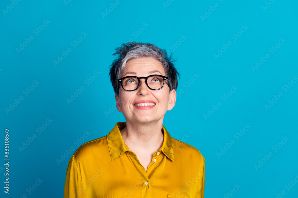 Wall mural Photo of adorable good mood lady dressed shirt eyewear smiling looking up empty space isolated blue color background