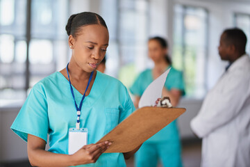 Focused Nurse Reviewing Patient's Medical Records in Hospital with Diverse Medical Team in Background