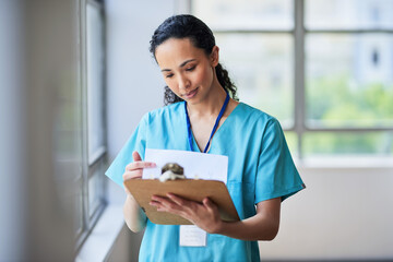 Focused Nurse Reviewing Patient Records On Clipboard In Hospital