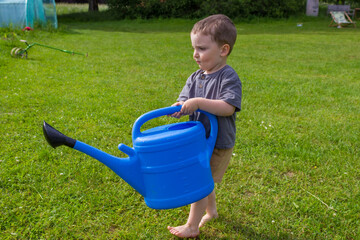 The boy watering vegetable garden from a watering can near a greenhouse