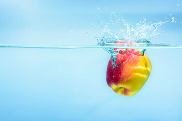 Red&yellow color ripe apple falling on water surface, concept of refreshment and relaxation in...