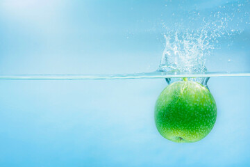 Green ripe apple falling on water surface, concept of refreshment and relaxation in health care