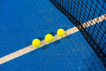 several balls by the net on a blue paddle tennis court