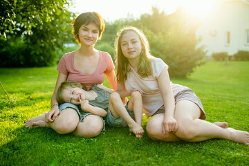 Cute big sisters cuddling with their toddler brother. Adorable teenage girls hugging their small sibling. Children exploring nature.