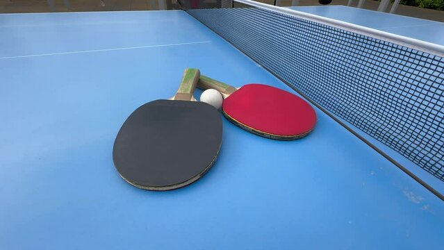 Two table tennis rackets lie on a blue tennis table, covering a white ball. Ping Pong. 