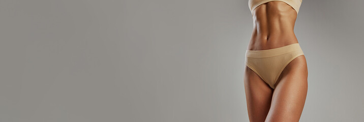 Banner. cropped portrait of fit female stomach against grey studio background with negative space...