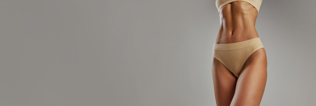Banner. cropped portrait of fit female stomach against grey studio background with negative space to insert your text. Concept of beauty and fashion, female health, anti-cellulite, dieting. Ad