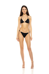 Young brunette woman in bikini swimsuit posing on a white studio background. Front view