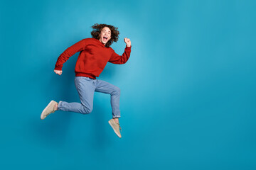 Full length photo of excited positive guy dressed red pullover jumping high running emtpy space...