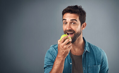 Portrait, man and eating apple for nutrition, healthy diet or wellness isolated on gray studio...