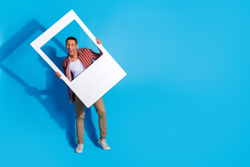 Photo of optimistic guy wear striped stylish shirt over white t-shirt hold photo frame winking eye...