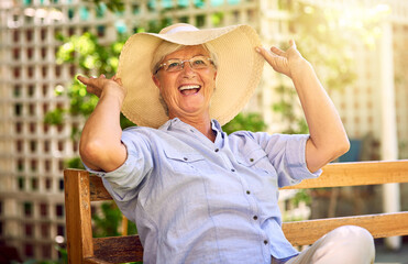 Portrait, laugh and senior woman with hat on bench, relaxation and glasses in garden. Joke, seat...