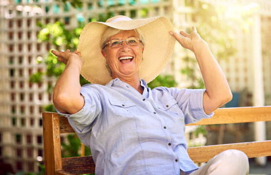 Portrait, laugh and senior woman with hat on bench, relaxation and glasses in garden. Joke, seat and elderly female person in backyard for happiness, comedy and funny with retirement in Canada