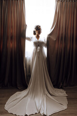 A woman in a long white dress stands in front of a curtain