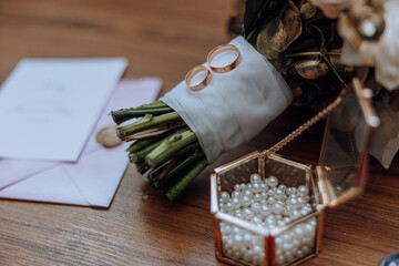A bouquet of flowers and a box of pearls are displayed on a wooden table. The flowers are arranged...