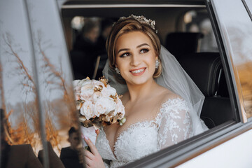 A bride is sitting in a car with a bouquet of flowers in her lap. She is smiling and looking out...