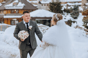 A bride and groom are standing in the snow, the bride is wearing a white dress and the groom is...