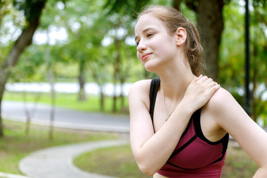 young woman in sports bra touches her shoulder in pain or injury while jogging in a park at the morning. fitness, health, injury, exercise and outdoor activities.