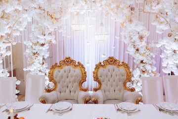 A white and gold decorated room with two chairs, one on each side of a table. The chairs are...