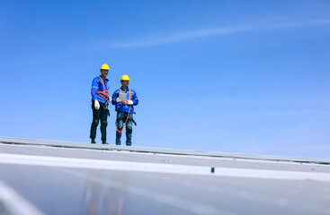 Two young engineers using tablet to inspect the area for installing additional solar panels on the roof of industrial factory.