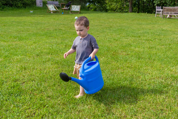 The boy watering vegetable garden from a watering can near a greenhouse