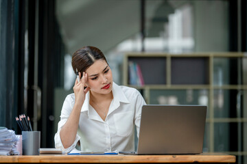 A woman is sitting at a desk with a laptop and a stack of papers