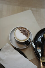 Coffee hot cappuccino black cup whipped cream with plate fork tissue on table in cafe brown tone.