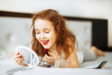 Kids makeup. Happy cute girl doing makeup lies on bed in the bedroom.