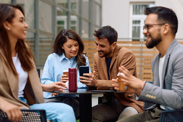 Happy colleagues using smart phone during coffee break at work.