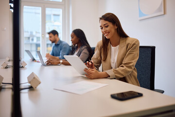 Happy businesswoman using digital tablet in shared workspace.