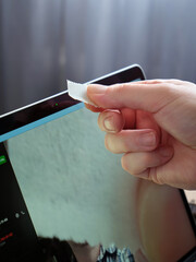 Vertical image close-up of a male hand covering the webcam on a laptop with a piece of paper.