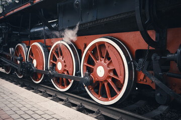 Close-up of a steam locomotive wheel at a railway station.