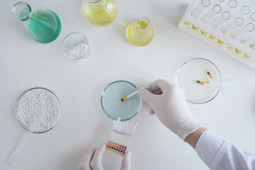 A chemist scientist tests the acidity of a liquid in a petri dish using litmus paper in a...