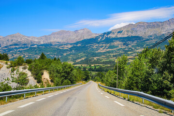Fototapeta premium Road winding above the shores of the Lake of Serre-Ponçon in the French Alps, a dammed artificial reservoir gathering the water of the Durance river