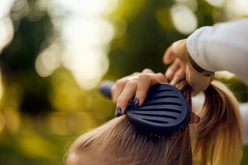 Close-up of a mother hands doing her daughter a hair, using a comb.