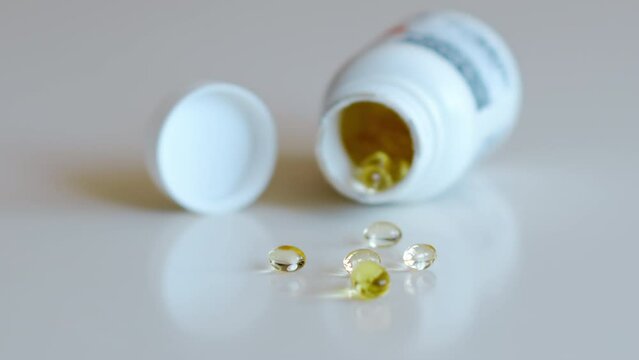 Fish oil omega 3 supplements spilling out of a packer bottle on a white background