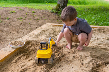  A little boy is playing with a toy dumper in the sand.