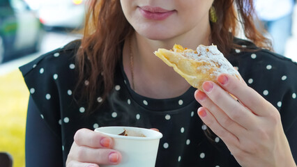 close up of woman drinking coffee from paper cup and eating bakery outside