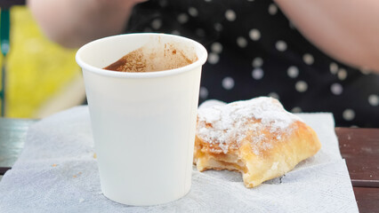 close up of woman drinking coffee from paper cup and eating bakery outside