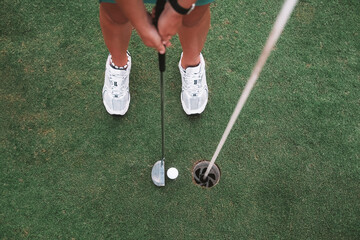 Top close-up view of the legs of a young woman playing golf on the green lawn of a country club. She hits the ball with a golf club and it rolls into the hole. A luxurious summer sport.