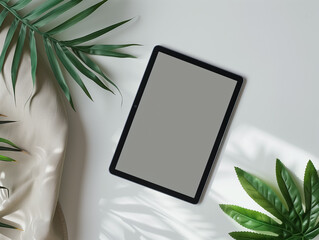 Digital tablet with blank screen on white background surrounded by green leaves, flat lay design for technology or nature concept.