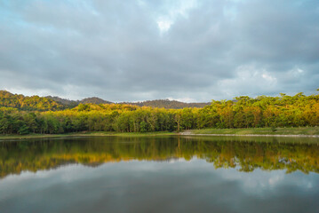 Beautiful nature lake and forest , Jet Khot Nature Study Centre lake and forest in Thailand. Beautiful view of a golden sun shining over a reflective lake under a cloudy sky after sunrise