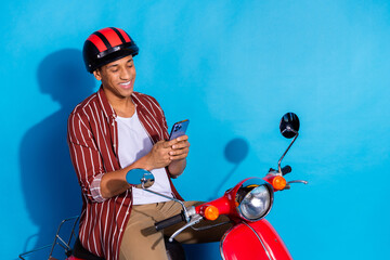Photo of cool optimistic guy wear striped stylish t-shirt helmet sit on moped look at smartphone...