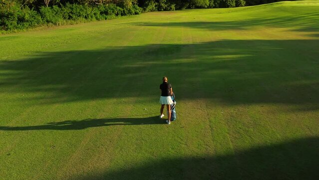 Aerial view of the green lawn at a golf country club where a young female professional golfer is playing. She came to the field with a bag containing golf clubs and balls.