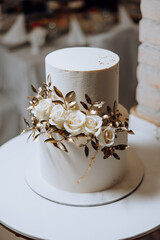 A white cake with gold leaves and white roses on top