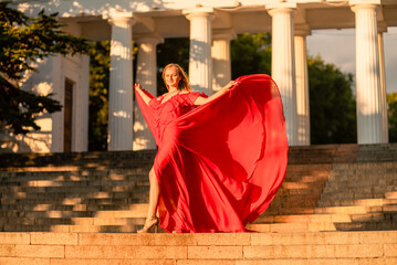 A woman in a long red dress against the backdrop of sunrise, bright golden light of the sun's rays....