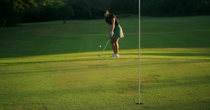Young woman at a country club taking a golf lesson. A beginner golfer takes a swing and hits the ball, but misses the hole. She is upset but does not lose her positive attitude and smiles.