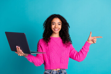 Photo portrait of lovely teen lady hold netbook point empty space dressed stylish pink garment isolated on cyan color background
