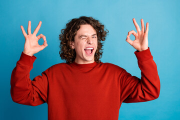 Photo of handsome good mood guy wear red sweater winking showing two okey signs emtpy space...